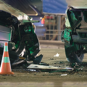 Severely damaged rear of a car after a serious nighttime auto accident with a traffic cone.