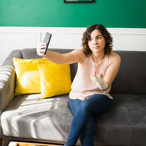 California Injury Claims: A person with a bandaged arm taking a selfie while sitting on a couch.