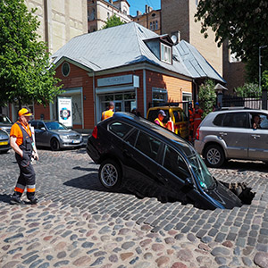 A car fallen into a large sinkhole or trench in an LA street construction zone.